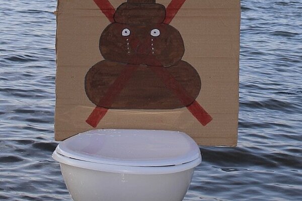 A toilet in the sea with a crossed through poo on a sign