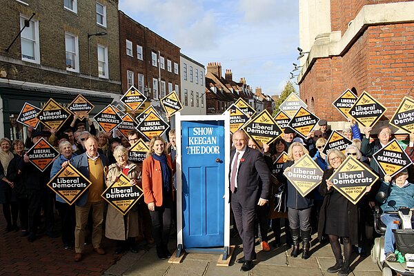 Sir Ed Davey, Jess Brown-Fuller and the Lib Dem team standing around a blue door labelled "Show Keegan the Door"